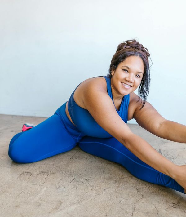 A smiling woman in comfortable sportswear stretching indoors.